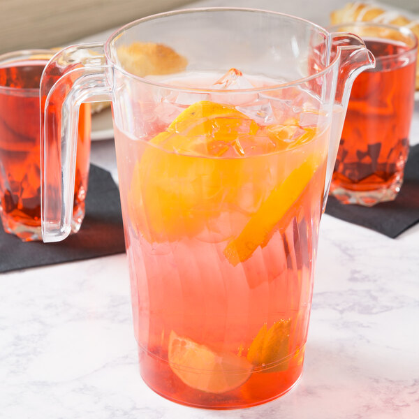 A clear Fineline plastic pitcher with pink and red liquid, orange slices, and a clear glass.