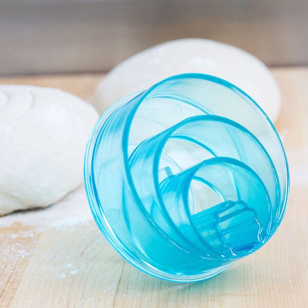 A blue plastic spiral Mexican bread stamp with a ring design on white dough.