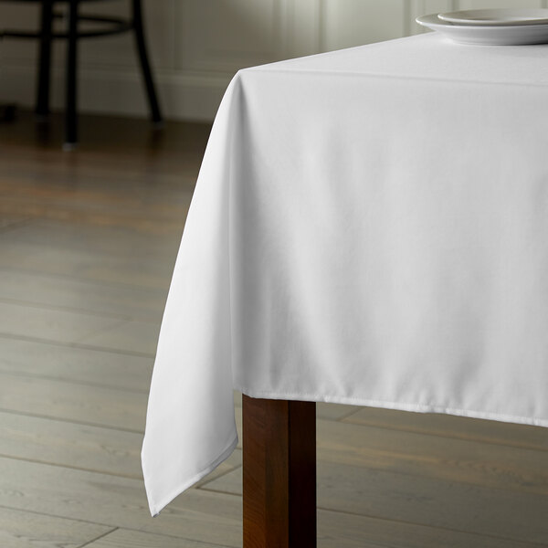 A wooden table with an Intedge white square tablecloth.
