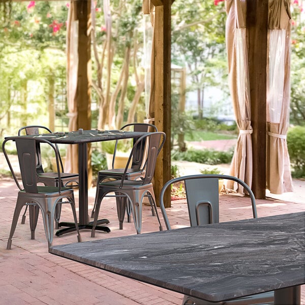 A Lancaster Table & Seating rectangular dining table with a smooth black finish and cross base plate on an outdoor patio.
