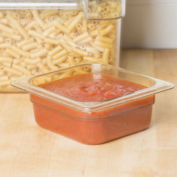 A Carlisle amber plastic food pan filled with pasta and sauce on a kitchen counter.