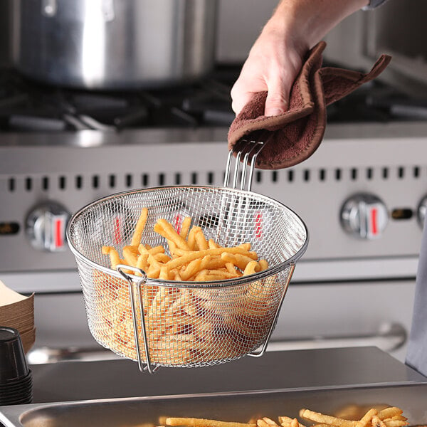A hand holding a Carlisle round steel mesh culinary basket filled with french fries.