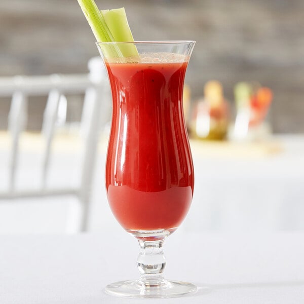 A Hurricane glass filled with red liquid and celery sticks.