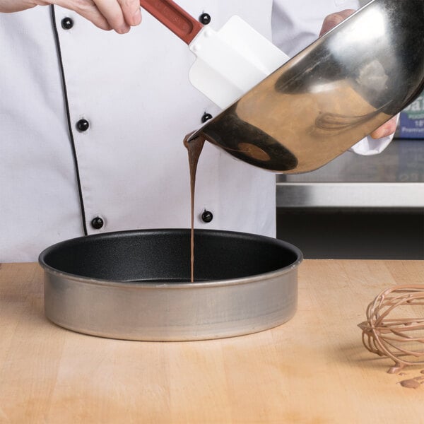 A chef pouring liquid chocolate into a Vollrath Wear-Ever round cake pan.