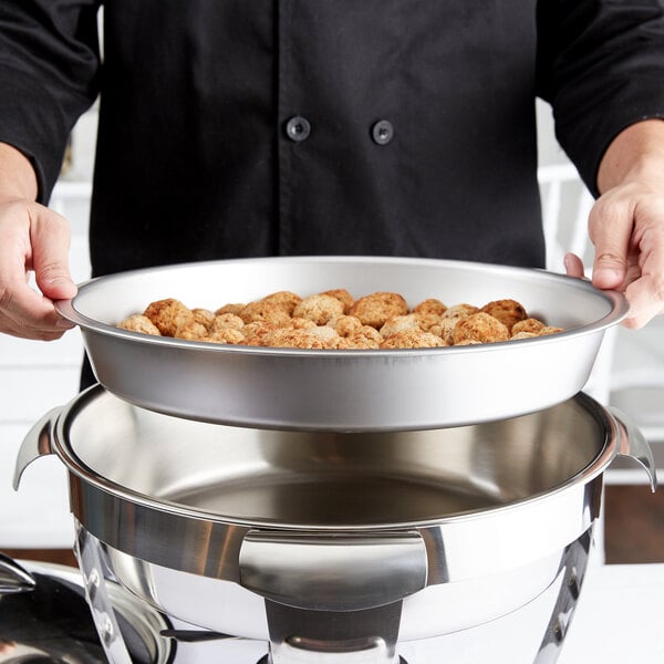 A chef holding a Vollrath stainless steel round food pan of food on a table outdoors.