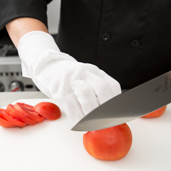 A person wearing a Victorinox cut-resistant glove cutting a tomato on a cutting board.