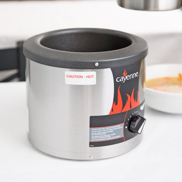 A Vollrath round soup warmer with a lid on a table with a bowl of soup inside.
