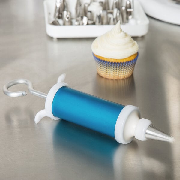 A cupcake with white frosting next to an Ateco cake decorating syringe on a table.