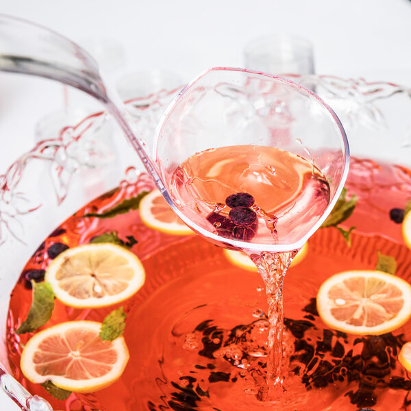 A Fineline clear plastic ladle pouring punch into a bowl of red punch with fruit.