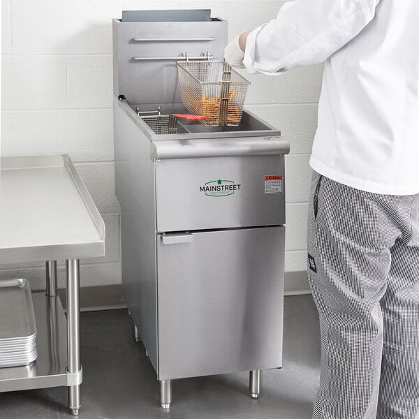 A person in a white shirt using a Main Street Equipment liquid propane stainless steel floor fryer to cook food.