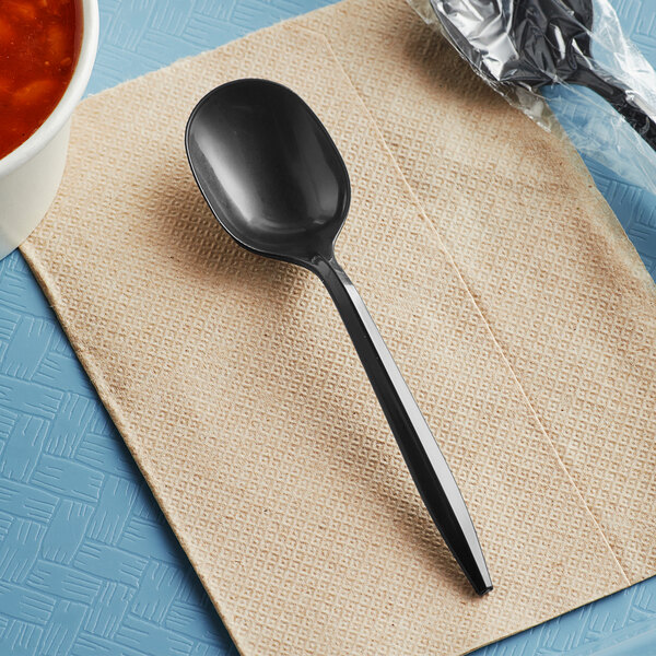 A black plastic soup spoon wrapped in plastic on a napkin.