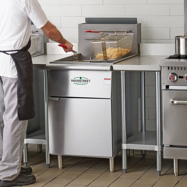 A man using a Main Street Equipment stainless steel floor fryer to cook food in a commercial kitchen.