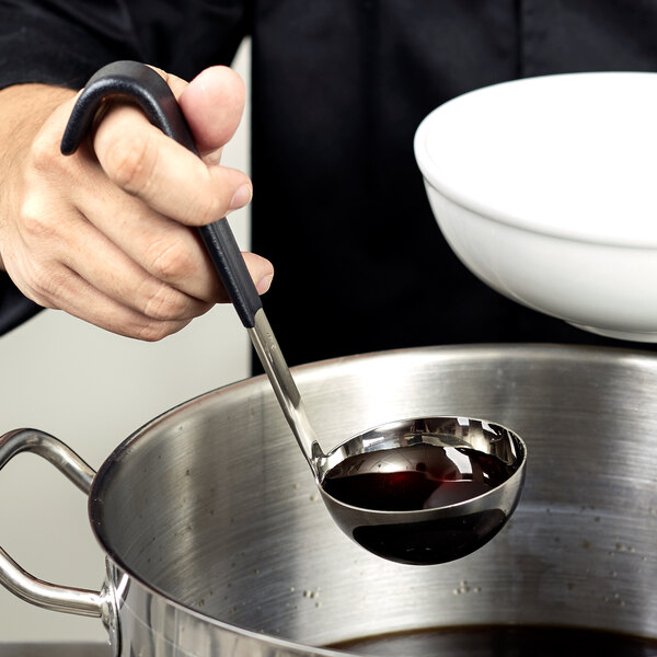 A person using a Vollrath Jacob's Pride ladle with a black Kool-Touch handle to pour liquid from a white bowl.