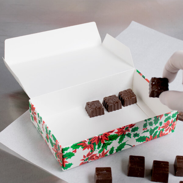 A hand holding a Poinsettia holiday candy box filled with chocolates.
