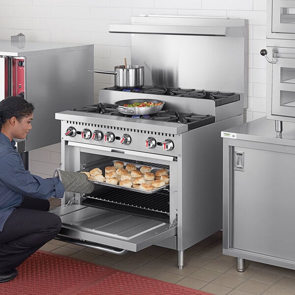 A man kneeling down in front of a Cooking Performance Group gas range in a professional kitchen.