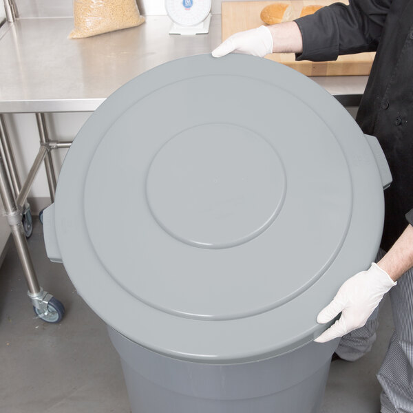A man in a chef's uniform holding a grey Continental Huskee trash can lid.