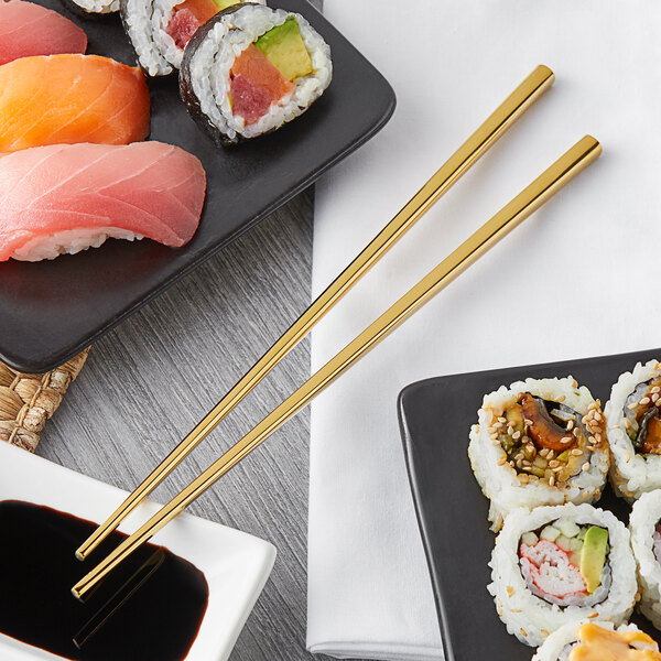 A plate of sushi rolls with Acopa gold stainless steel chopsticks on a table.