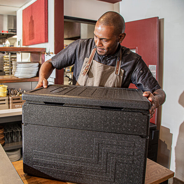 A man holding a large black Cambro Cam GoBox food pan carrier.