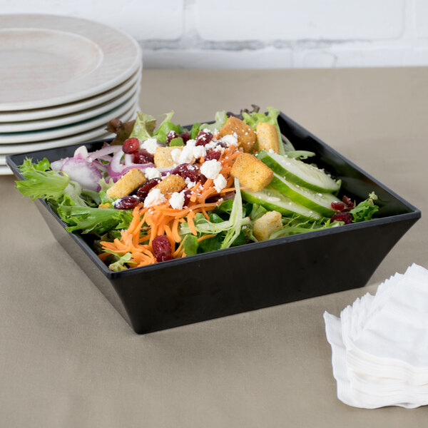 A salad in a black GET Siciliano square bowl with a napkin and a fork.