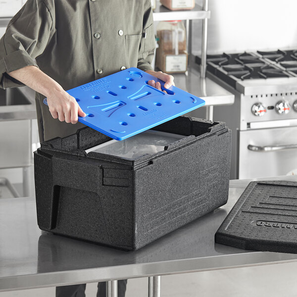 A woman using a Cambro Cam GoBox full size food pan carrier with a blue lid.