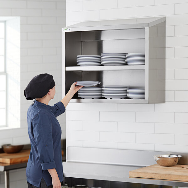 A woman in a chef's hat putting plates on a Regency stainless steel wall shelf.