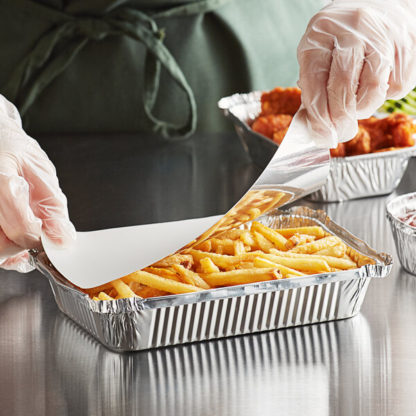 A person in white gloves putting food in a Choice oblong foil container.