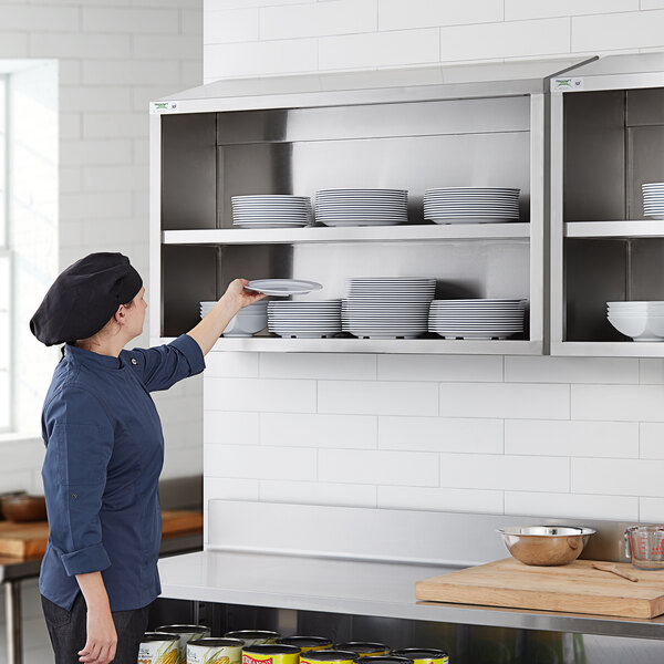 A woman in a kitchen putting plates on a Regency stainless steel wall shelf.