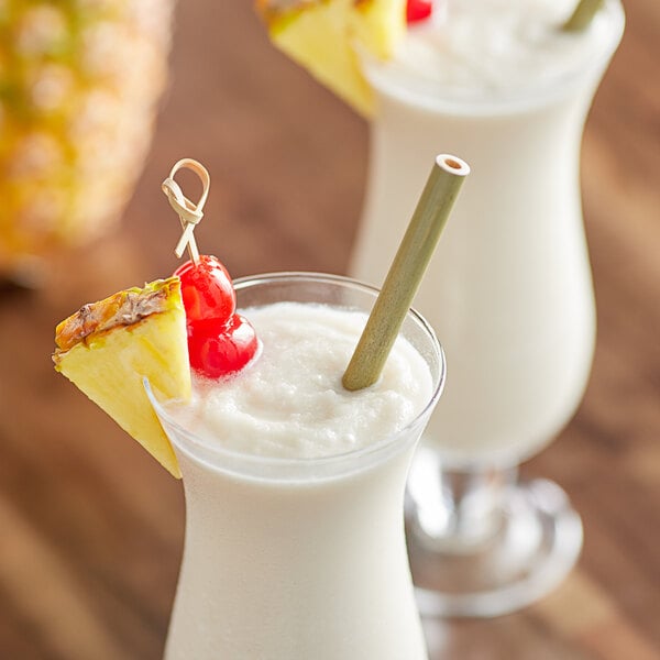 A glass of Island Oasis Pina Colada with a straw garnished with pineapple.
