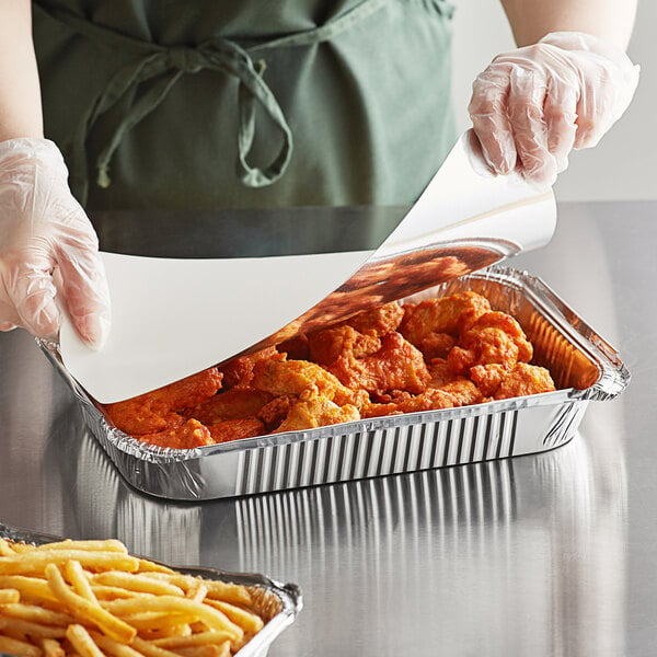 A person in gloves putting food in a Choice oblong foil tray.