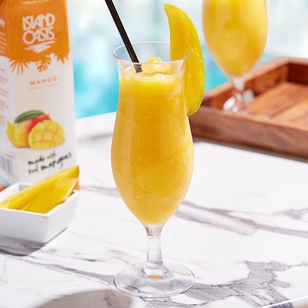 A glass of yellow Island Oasis mango beverage with a straw and a slice of mango on the rim.