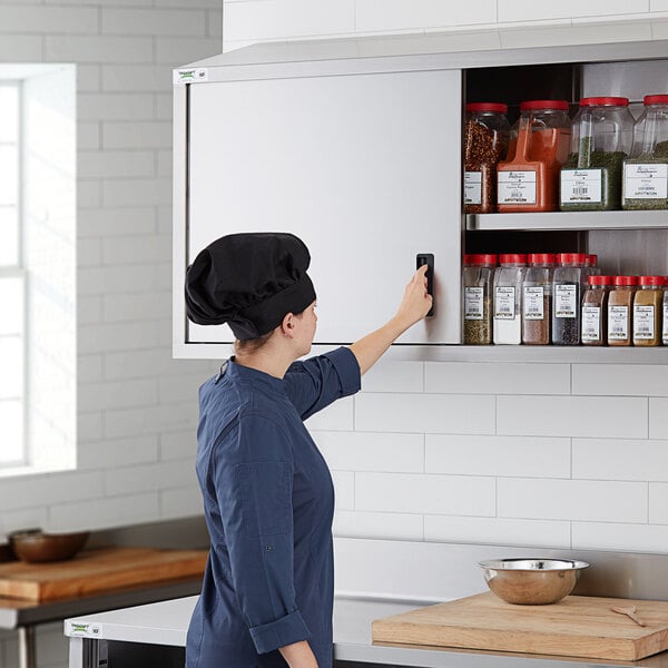 A woman wearing a chef's hat opening a Regency stainless steel wall cabinet.