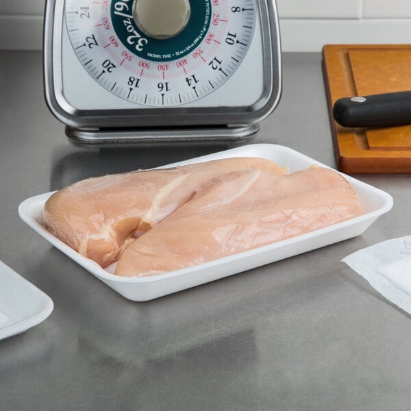A white CKF foam meat tray with raw chicken breast on a scale.