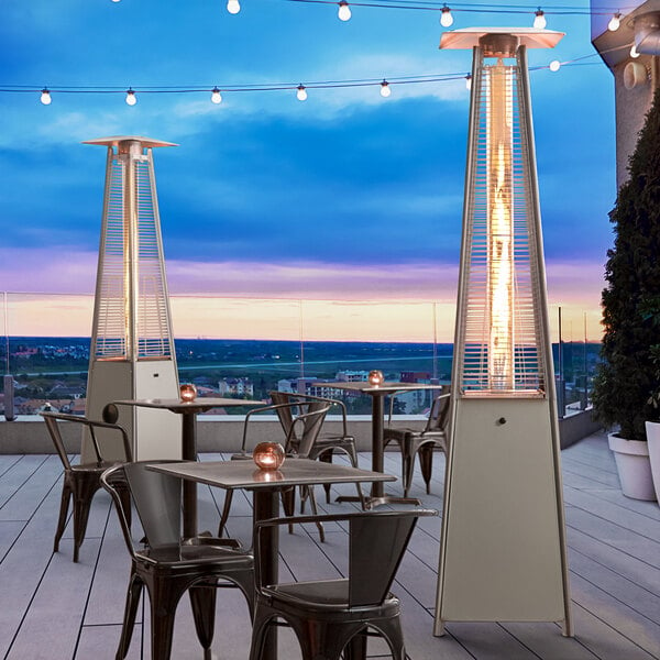 A Backyard Pro steel patio heater with a glass tube on an outdoor patio with tables and chairs.