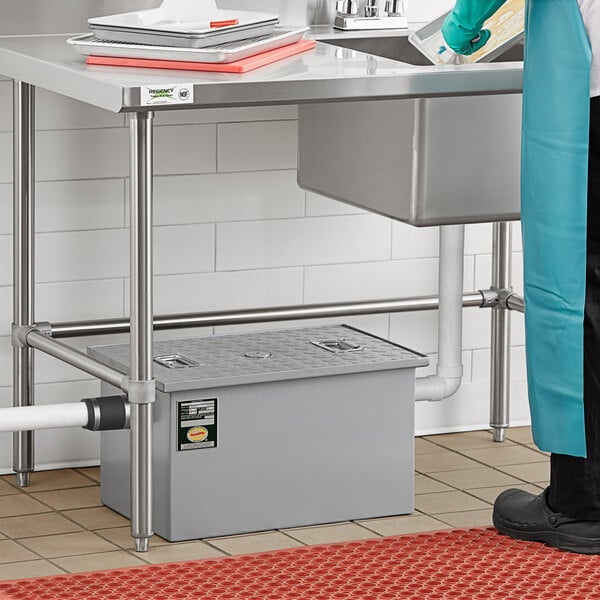 A person in a blue uniform using a Regency 20 lb. Grease Trap on a counter in a school kitchen.