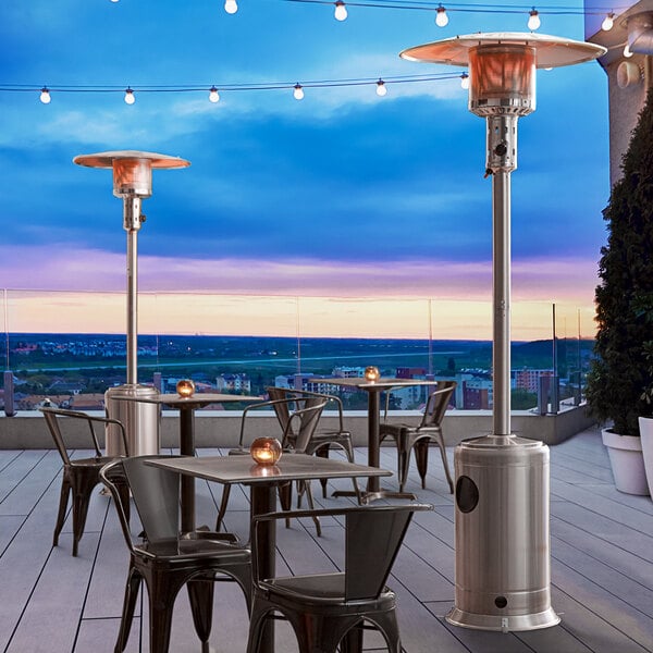 A stainless steel Backyard Pro portable patio heater on an outdoor patio with a table and chairs.