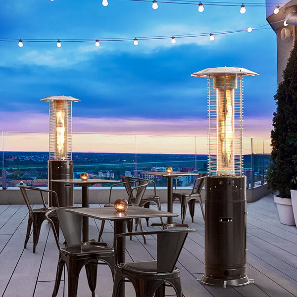 A black Backyard Pro portable patio heater with a glass tube on a table with chairs on a deck.