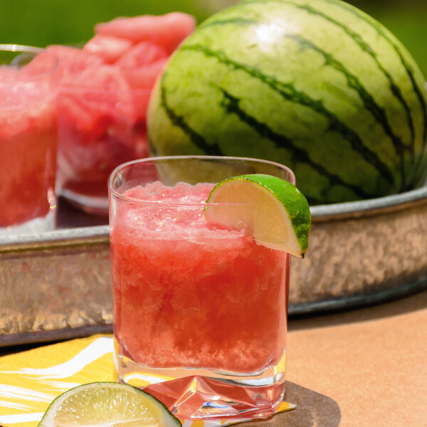 A Luigi Bormioli Strauss juice glass filled with watermelon juice and a lime slice on a table.
