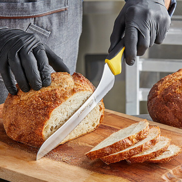 A person using a Dexter-Russell yellow handled knife to slice a loaf of bread.