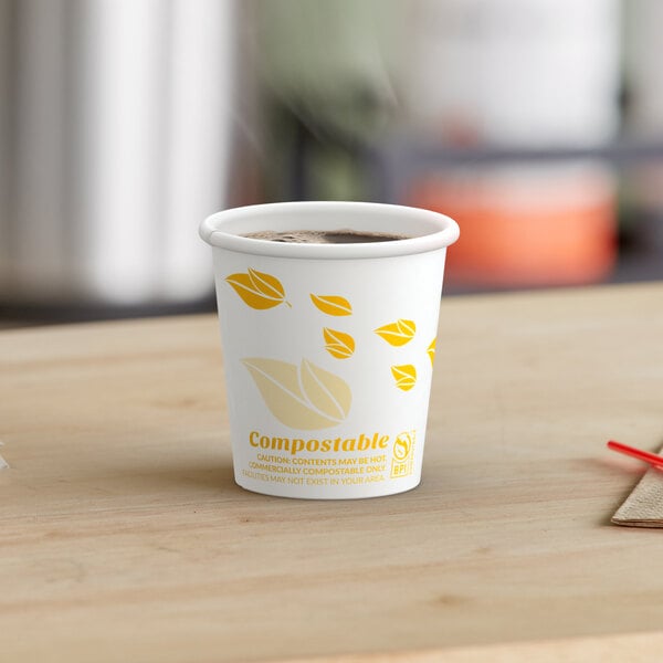 A table with a cup of coffee in a EcoChoice Leaf Print paper cup with brown liquid.