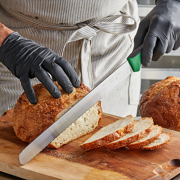 A person wearing black gloves slicing bread with a Dexter-Russell scalloped bread knife on a cutting board.