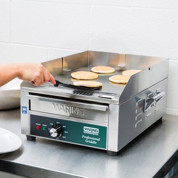 A woman using a Waring countertop griddle to cook pancakes.