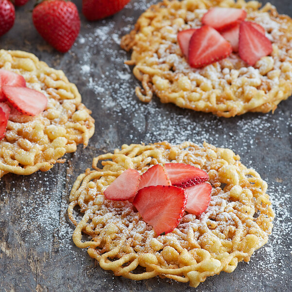 A table with three funnel cakes topped with strawberries and powdered sugar.