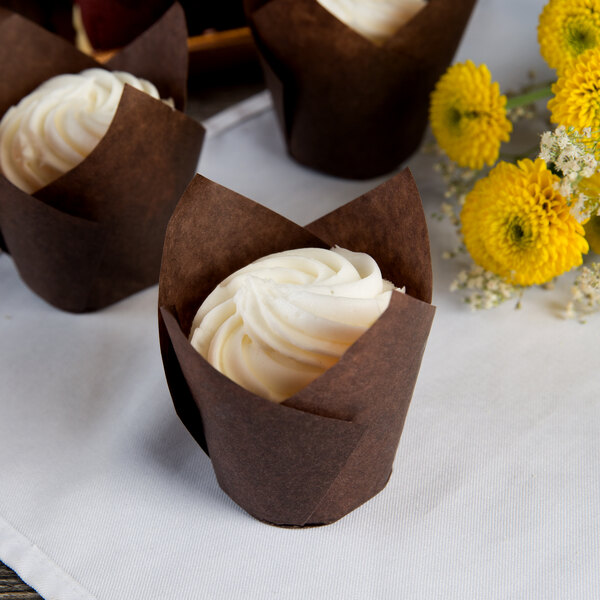 Hoffmaster chocolate brown tulip baking cups on cupcakes with white frosting next to yellow flowers.