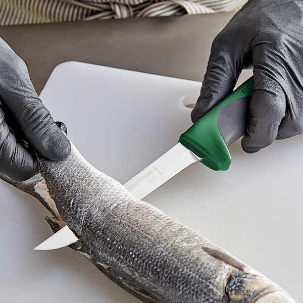 A person in a glove using a Dexter-Russell narrow boning knife with a green handle to cut fish.