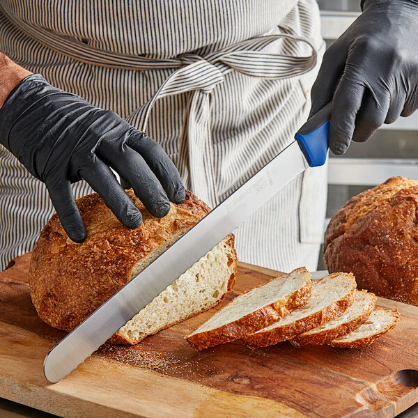 A person wearing black gloves uses a Dexter-Russell scalloped bread knife to slice a loaf of bread on a cutting board.