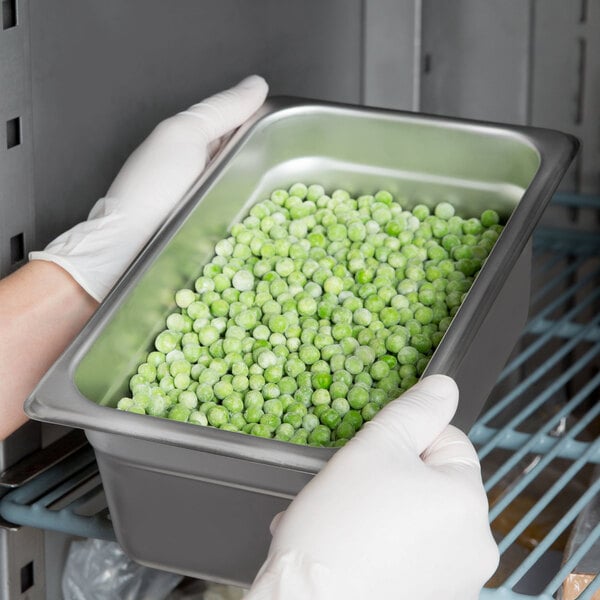 A person in gloves holding a Choice stainless steel steam table pan filled with peas.