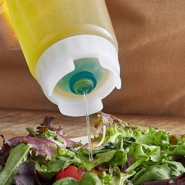 A person using a FIFO Innovations thin squeeze bottle lid to pour yellow liquid onto a salad.