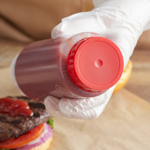 A hand in white gloves using a FIFO Innovations Red Cap on a plastic squeeze bottle of sauce.