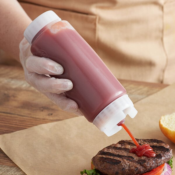 A person using a FIFO Innovations double wide-mouth squeeze bottle to pour ketchup on a burger.