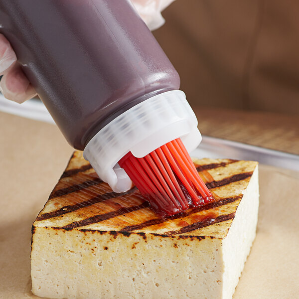 A person using a FIFO Innovations basting brush cap to put sauce on a piece of food.